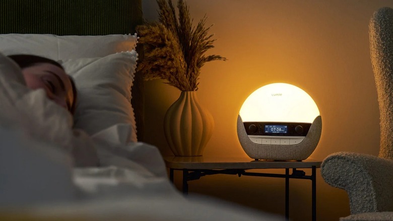A spherical sunrise alarm clock on a nightstand next to someone sleeping in bed
