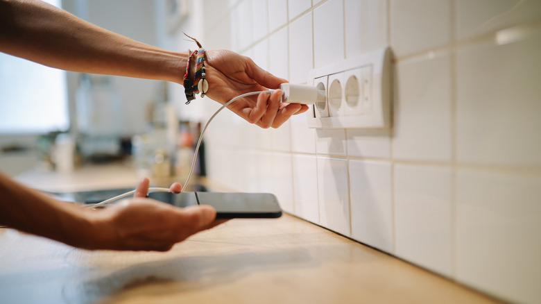 Someone plugging USB phone charger into a kitchen wall outlet.