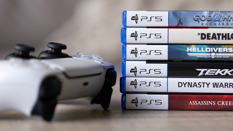 a stack of PlayStation 5 game cases next to the PlayStation 5 controller
