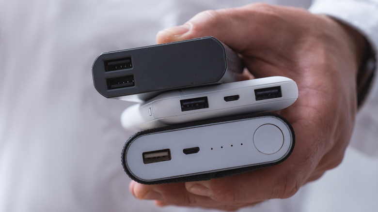 A hand holding three portable chargers.
