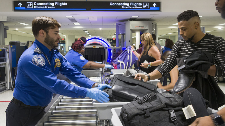 A TSA agent helping a man put his bag in a tray at airport security.