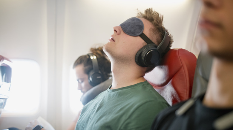 A person wearing an eyemask and headphones, asleep on a plane