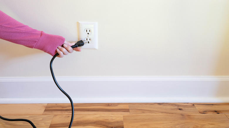 Someone's hand plugging in a power cord into a wall outlet.