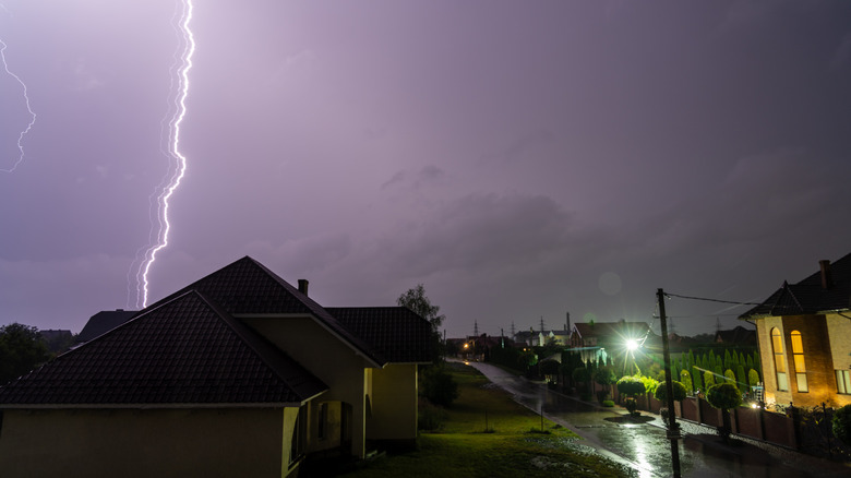 Lightning strike visible behind a residential street at night.