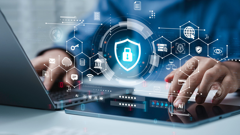A man works on a laptop and tablet, with many antivirus security symbols displayed over his hands.
