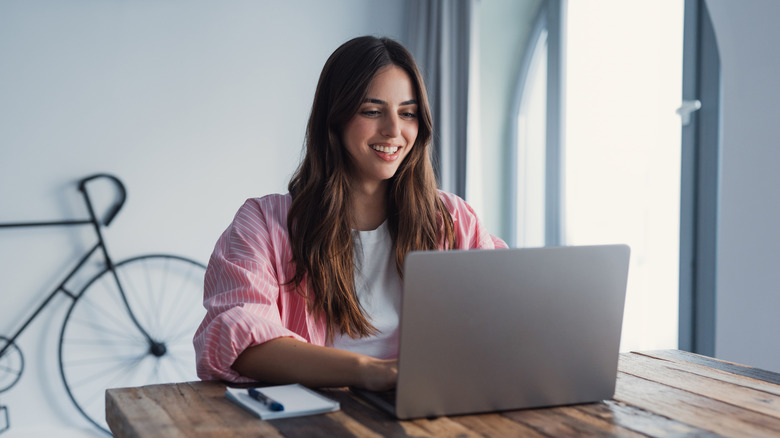 Happy young woman sit at desk look at laptop screen browsing surfing wireless Internet at home