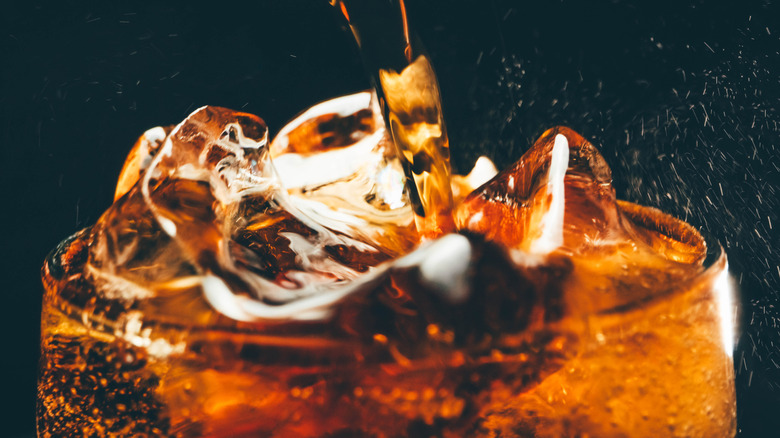 brown soda being poured into a glass with ice cubes