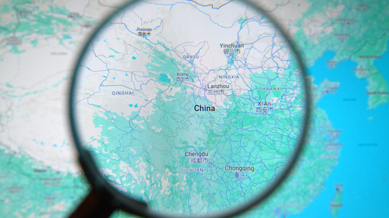A person looking through a magnifying glass at a screen displaying Google Earth data for China.