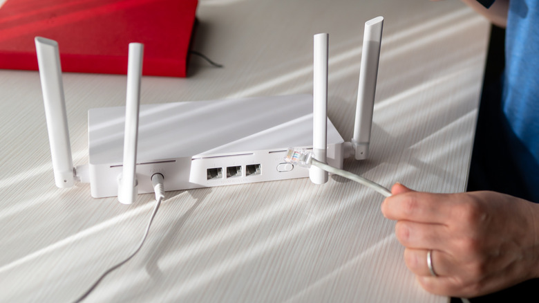 Close-up of a person holding an Ethernet cable to connect to a router placed on a wooden desk