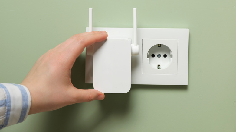 Hand turning on a Wi-Fi extender at the plug socket