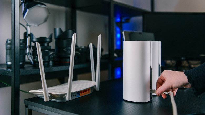 Person plugging in a mesh node with a router beside it on the table