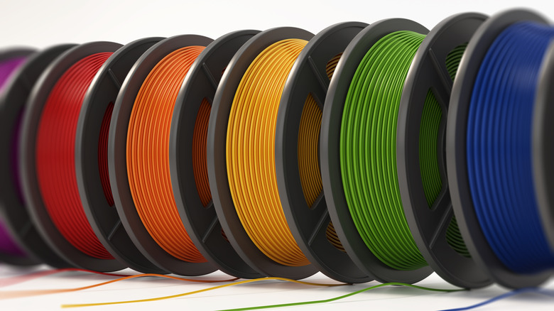 A series of 3D printing filaments, featuring from left to right: Purple, red, orange, orange, green, and blue