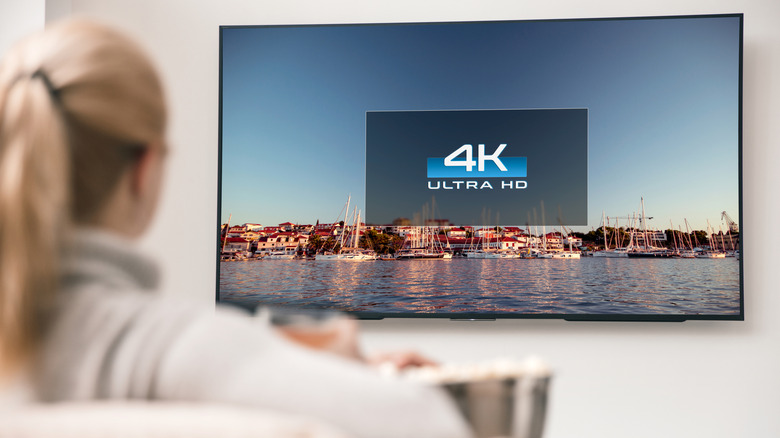 Woman on couch watching 4K UHD TV mounted on wall.