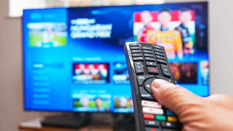 TV remote control in hand aimed at powered-on TV set.