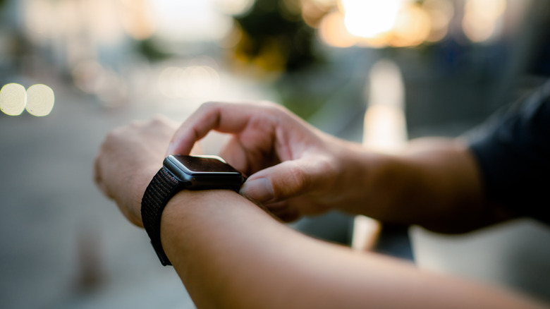 Close up of someone using a smartwatch outdoors with a blurry background.