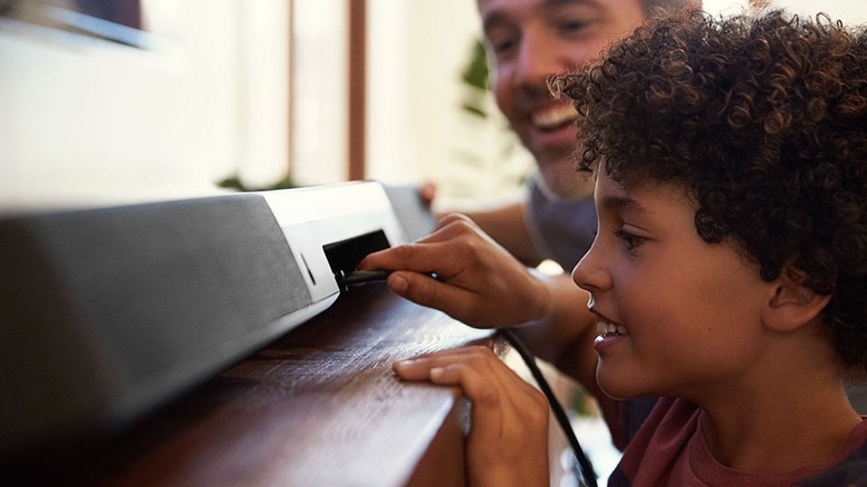 A child plugging an HDMI cable into a the back of a soundbar
