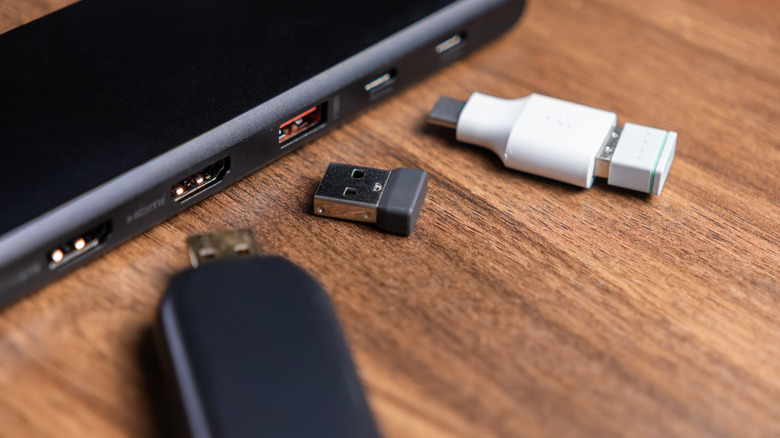 Three USB dongles placed in front of laptop ports on a brown wooden surface