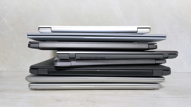 Eight laptops in various shades of gray and silver stacked atop one another against a light gray background