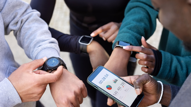 A close-up of a group of people looking at smartwatches, a smartphone, and an analog watch