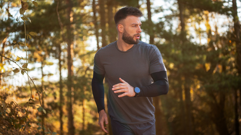 A man jogging in the woods wearing a smartwatch