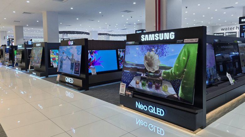 The inside of a shopping center or mall where there are televisions from Samsung, LG, and Sony, the TVs are separated by company down different aisles