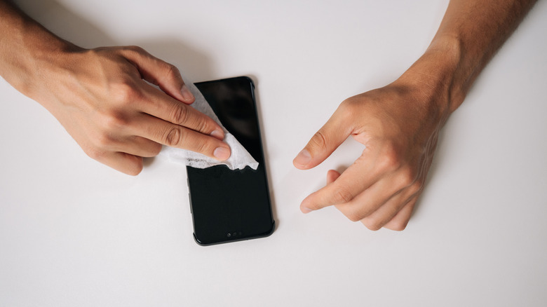 A person cleaning a smartphone display screen with a wipe.