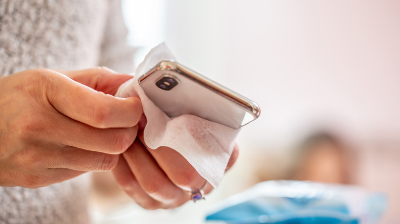 Hands cleaning the surfaces of a phone with a wipe.