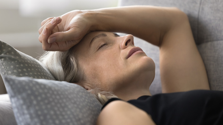 A woman lying on a sofa with her eyes closed and her forearm resting on her forehead.