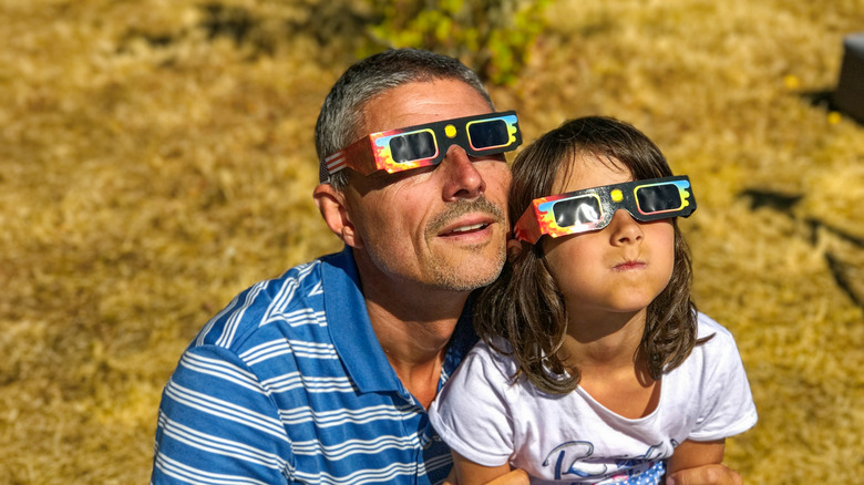 A man and a child wearing solar eclipse glasses.