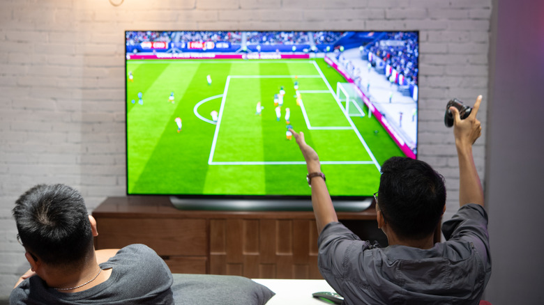 Two people sitting on a couch watching a soccer game on an LG OLED TV