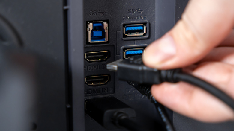 Person plugging in HDMI cable into back of display.