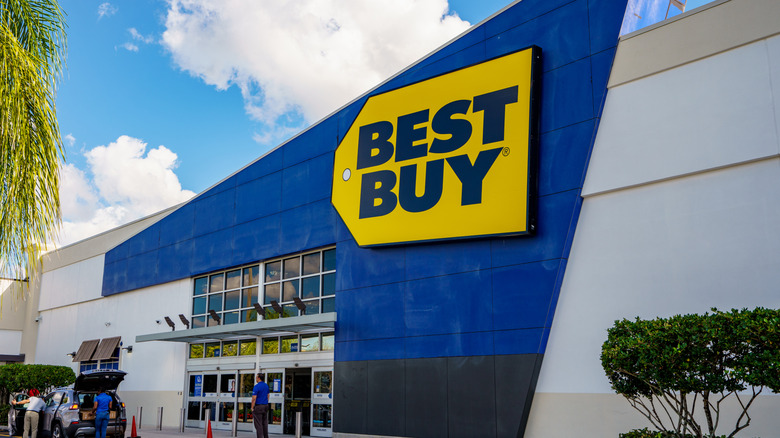 Front view of a Best Buy store. The Best Buy logo is written in a dark blue over a yellow background on a blue wall