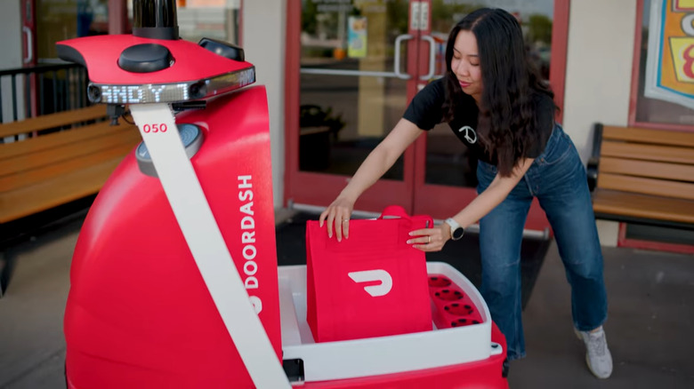 A woman loading an order in DoorDash's delivery robot, DoorDash Dot.