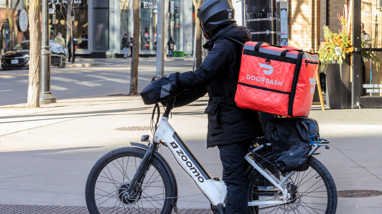A man in a coat, on an electric bike, delivering for DoorDash.