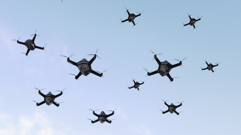 A swarm of quadcopter drones fly through a blue sky