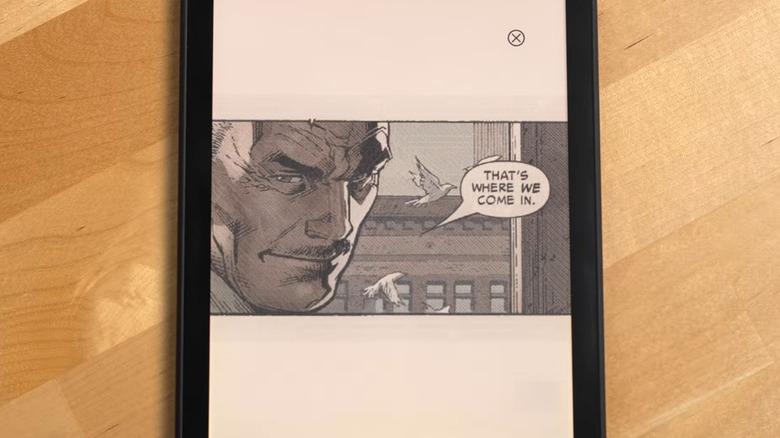 A Kindle color soft on a light brown wooden table shows a comic book panel with a man saying "That's where we come in" as birds fly in the background.