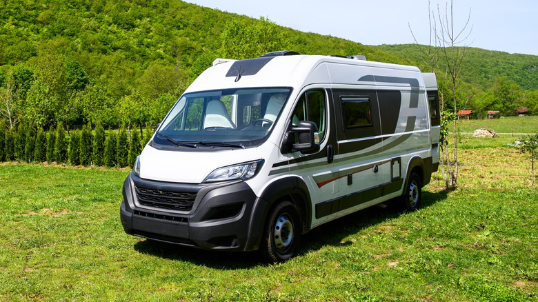 A white camper van sitting in the grass against large hills