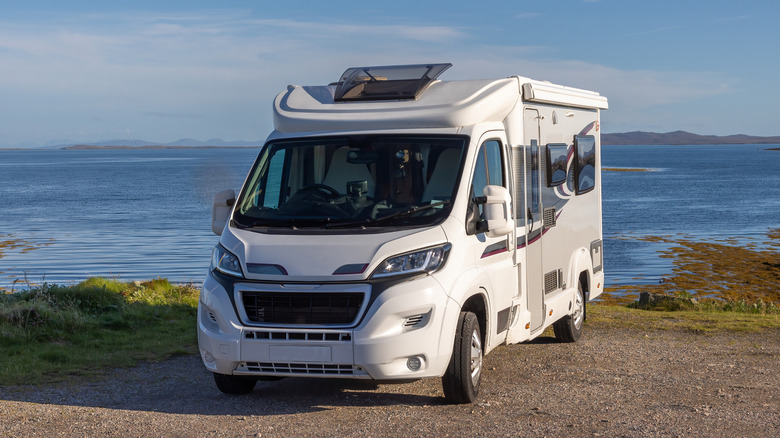 A white camper van facing the camera as it sits along the edge of the ocean