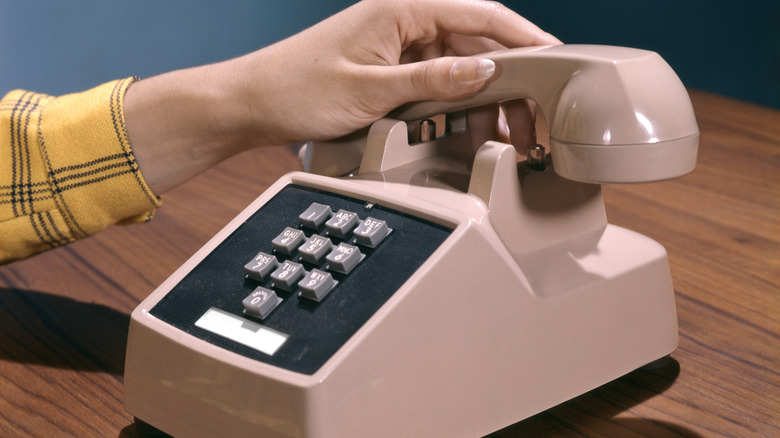 A hand picking up the receiver of a pink touch-tone phone