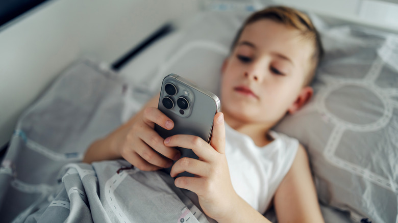 A young boy lying in bed with an iPhone in hand