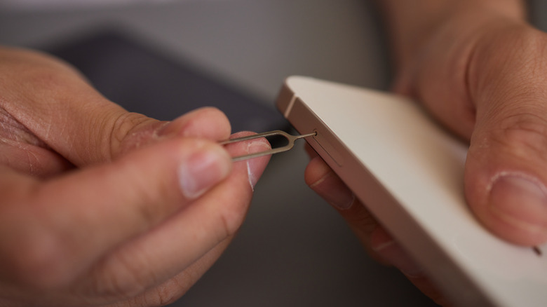 person insert sim removal tool into side of smartphone to change out physical sim card