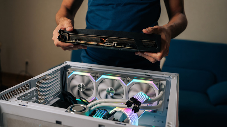 A person holding a graphics card over a custom PC that is currently running.