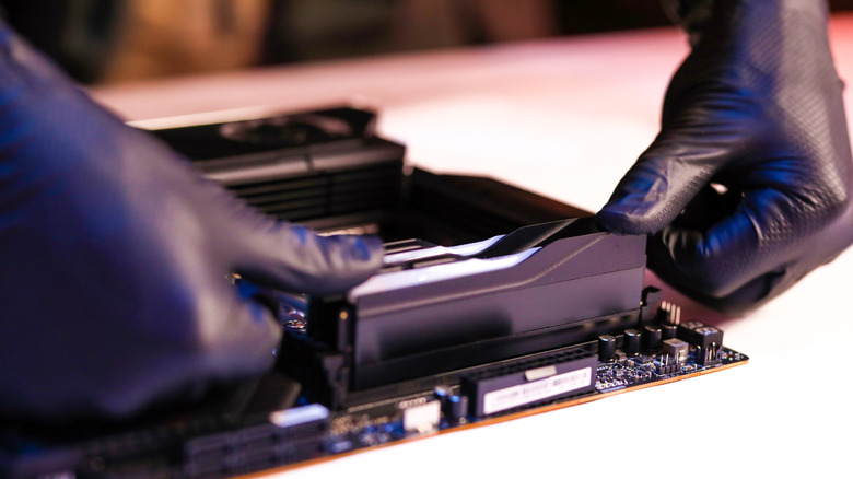 A close-up of a person installing RAM sticks into a desktop motherboard.