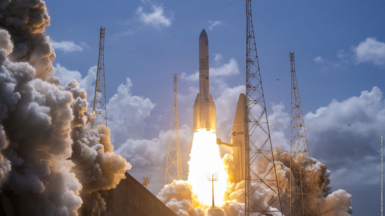 An Arianespace rocket blasts off, sending plumes of smoke into the sky.