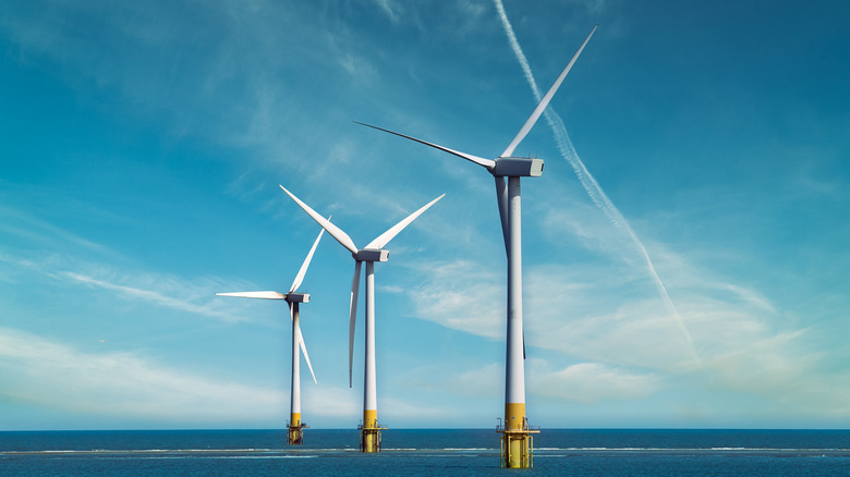 offshore wind turbines in a row, streaks of clouds across the sky in background