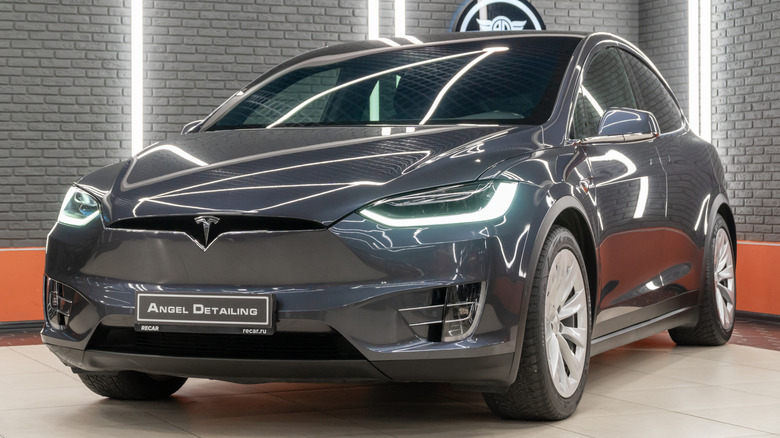 Gray Tesla Model Y parked inside a car detailing studio with its headlights on.