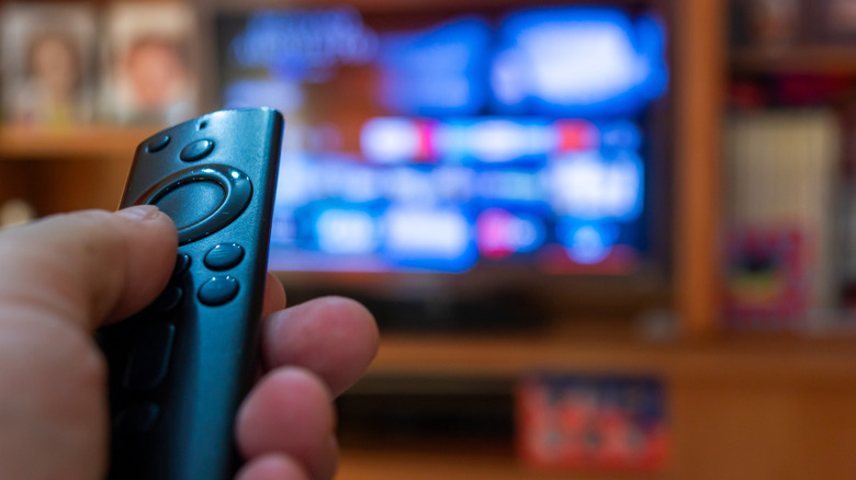 A hand holding an Amazon Fire TV Stick remote pointed at a TV