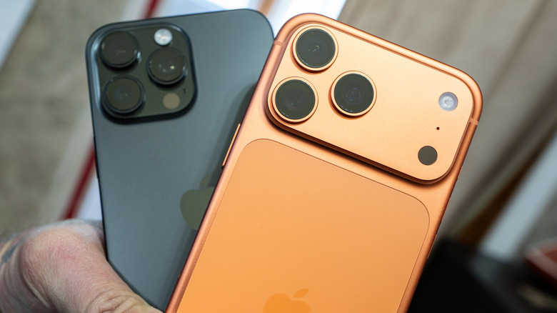 Hand holding black iPhone 16 Pro Max and orange iPhone 17 Pro Max