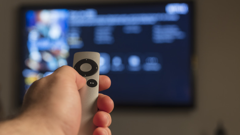 Man holding Apple TV remote control pointing at TV
