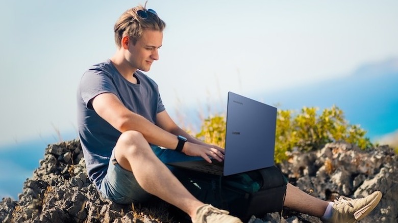 Man sitting on rocks using a Samsung laptop on his lap.